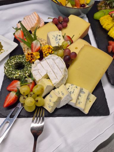 Ein Käsebrett mit verschiedenen Käsesorten, Trauben, Erdbeeren und essbaren Blüten.